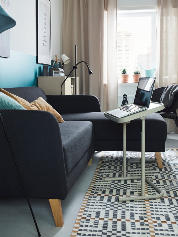 Un sofá LINANÄS el L en una sala con una mesa para notebook en frente.