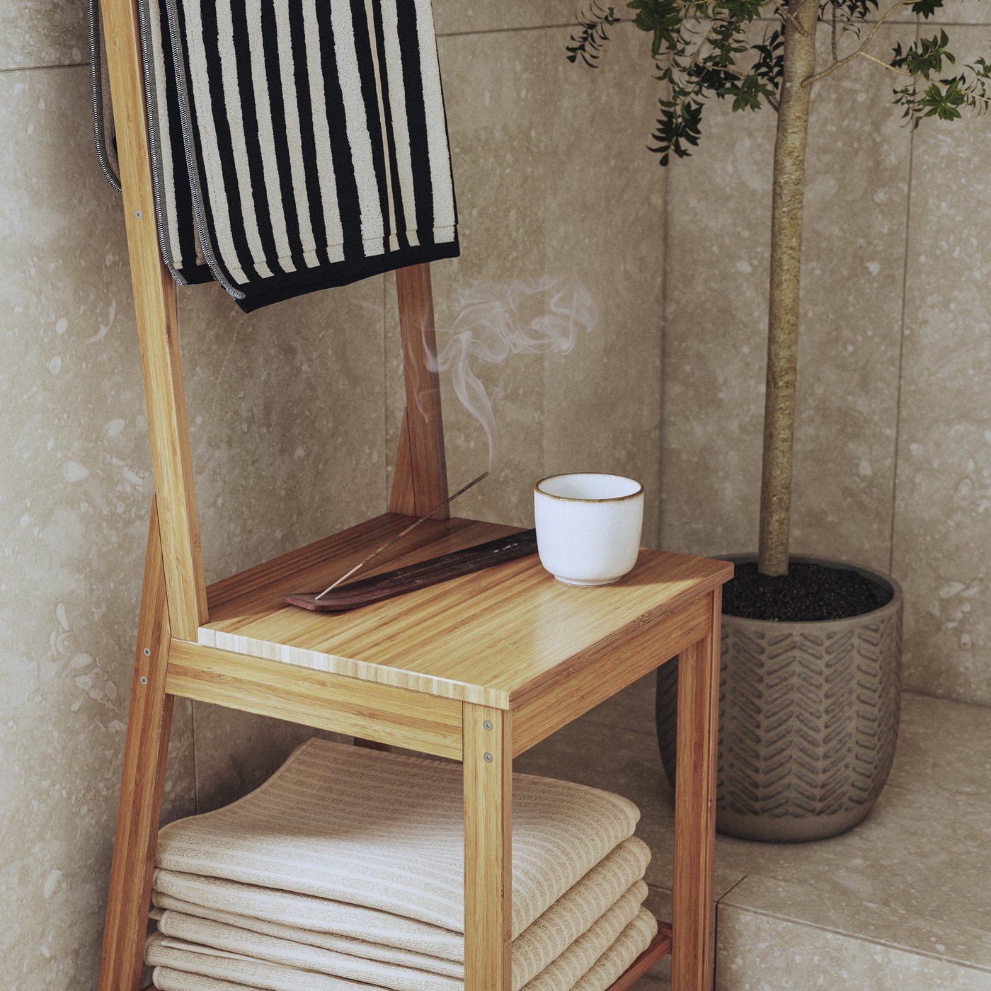 A RÅGRUND towel rack chair in bamboo with white and striped towels, a cup of tea and incense stick. A large plant next to it.