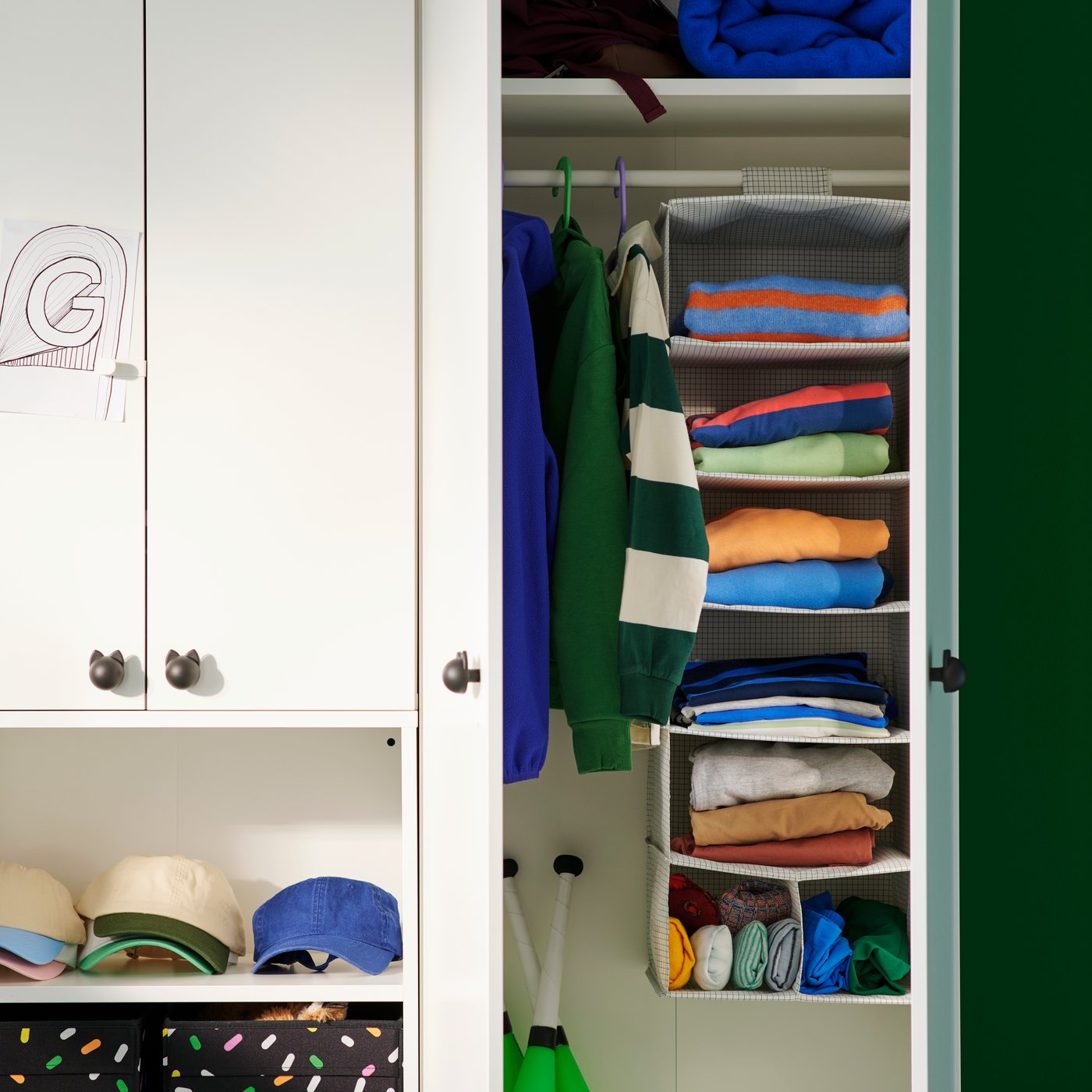 Inside a white wardrobe, a STUK hanging storage with 7 compartments holds colourful folded clothes in a children’s room.