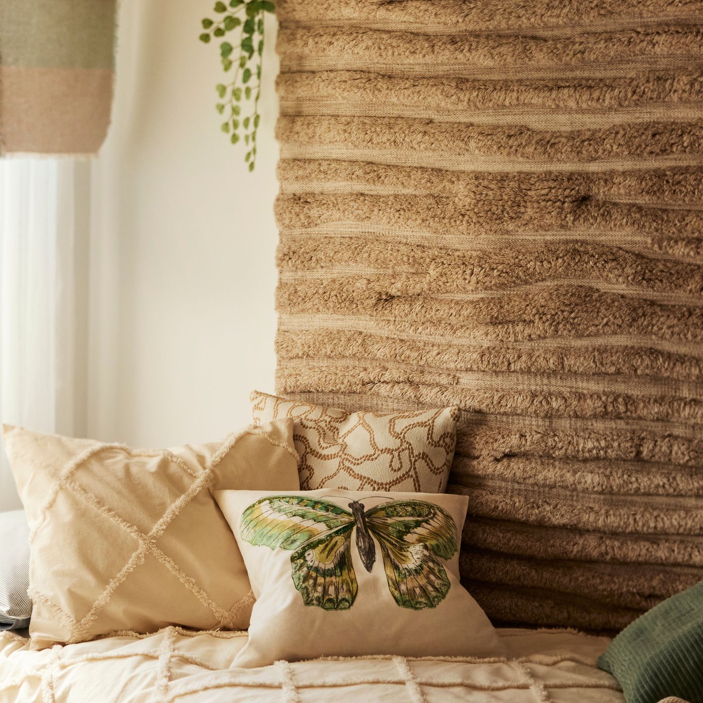 An der Wand eines Schlafzimmers im Bohème-Stil hängt ein handgewebter, beigefarbener BANKKONTOR Teppich mit Wellenmuster in Wolle über einem Bett mit Kissen.