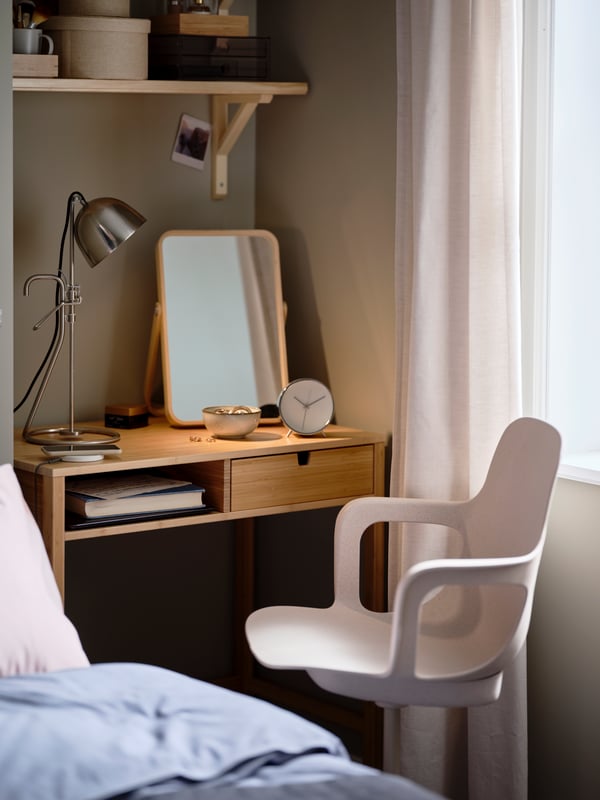 A bedroom with a BJÖRKSNÄS birch bed, dark-blue KOPPARBLAD bed linen, a NORDKISA dressing table, and an ODGER swivel chair.