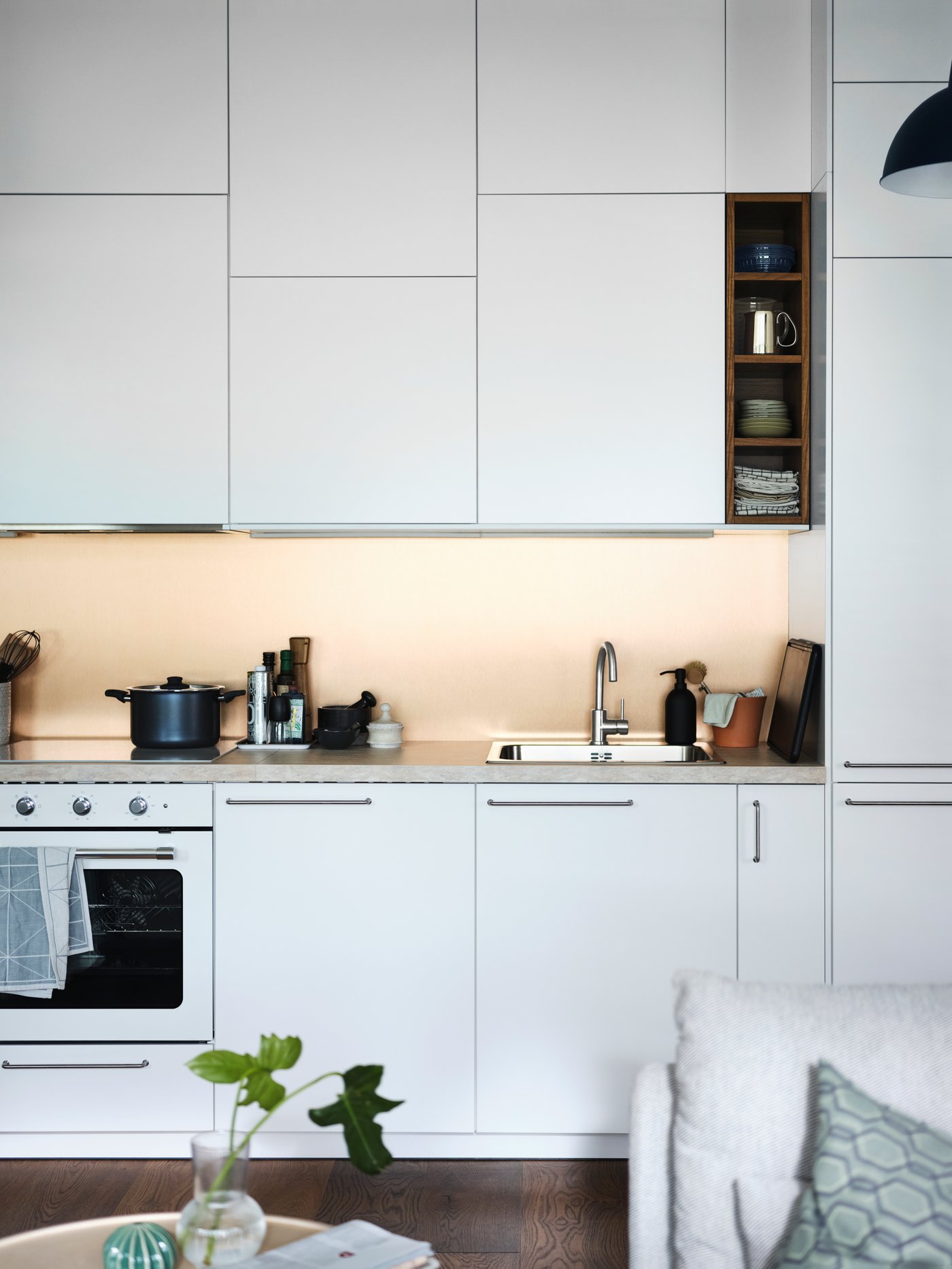 An open plan white METOD kitchen with a beige stone effect/laminate SÄLJAN worktop and a white MATTRADITION forced air oven.