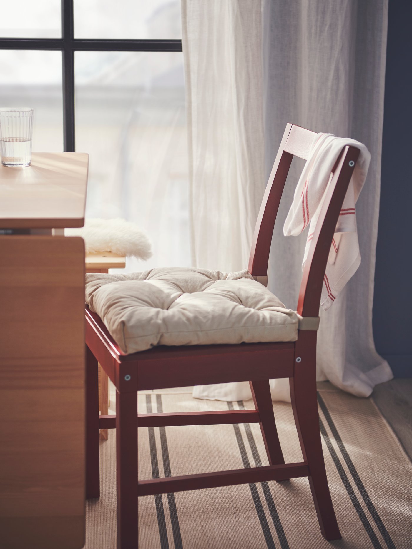 A red stained PINNTORP chair with a beige MALINDA chair pad in the dining room.