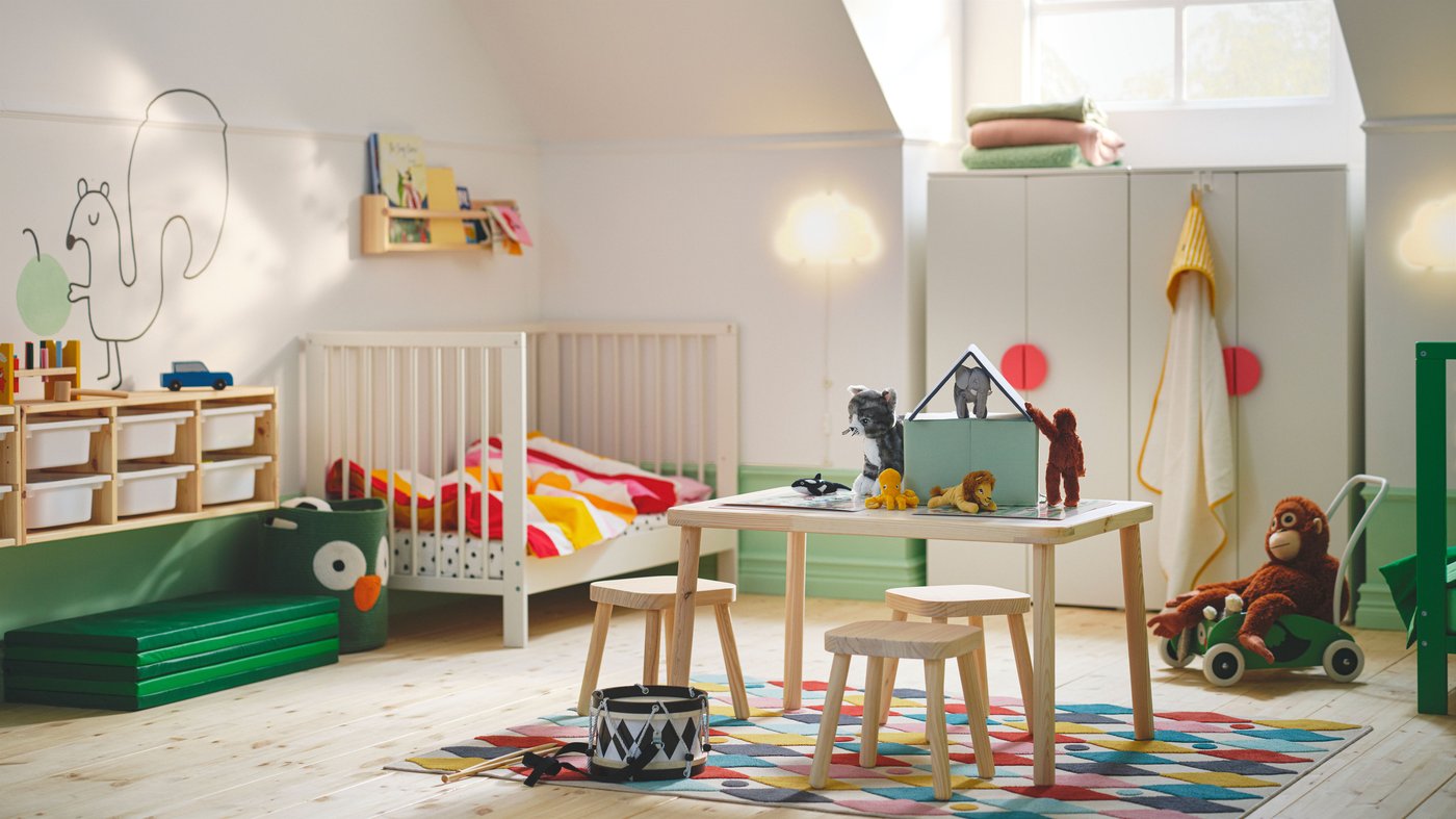A children’s room with a white GULLIVER cot in one corner and a FLSAT children’s table and three stools on a BUSENKEL rug.