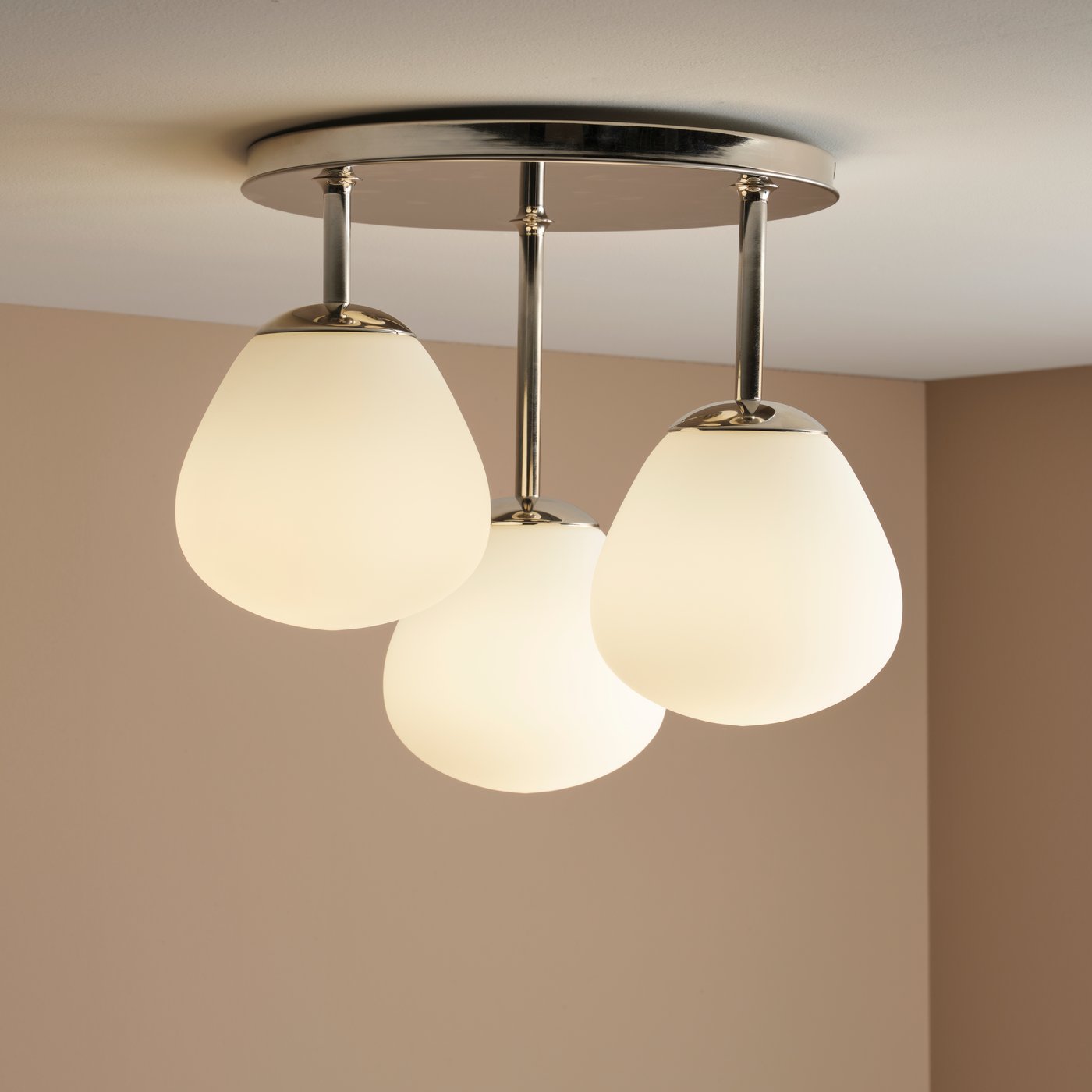 En DEJSA loftslampe i forkromet/opal hvidt glas med tre lamper er fastgjort til et hvidt loft i et rum med beige vægge.