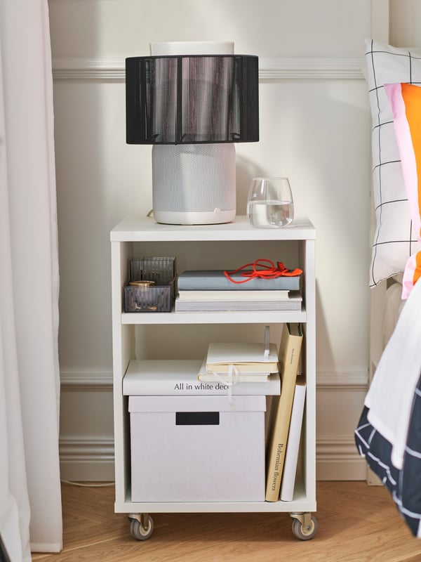 Close-up of white bedside table on wheels, with black and white SYMFONISK speaker lamp with wi-fi on top of it.