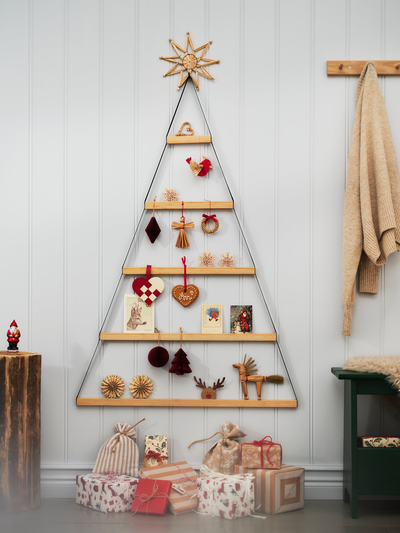 A triangular VINTERFINT wall decoration with bamboo shelves filled with Christmas decorations hangs above wrapped gifts.