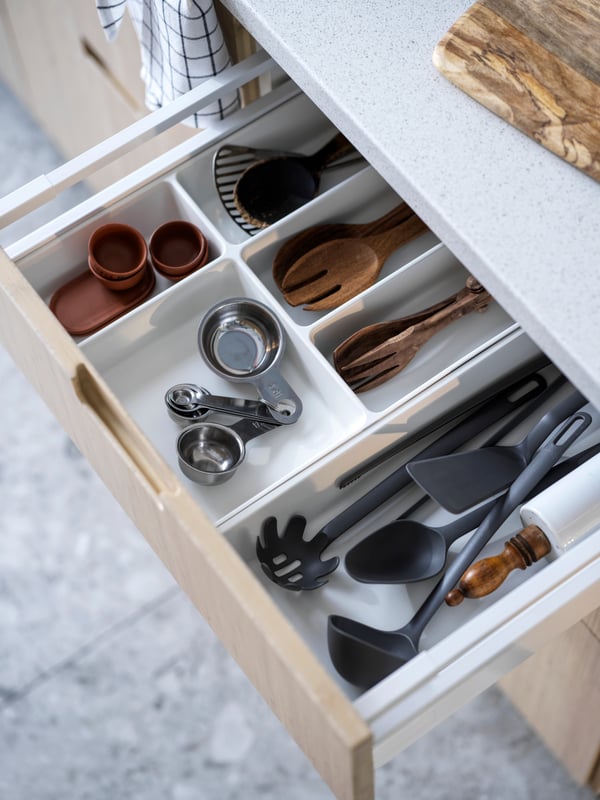 A pulled-out kitchen drawer revealing kitchen utensils in plastic and bamboo in UPPDATERA cutlery and utensils trays.