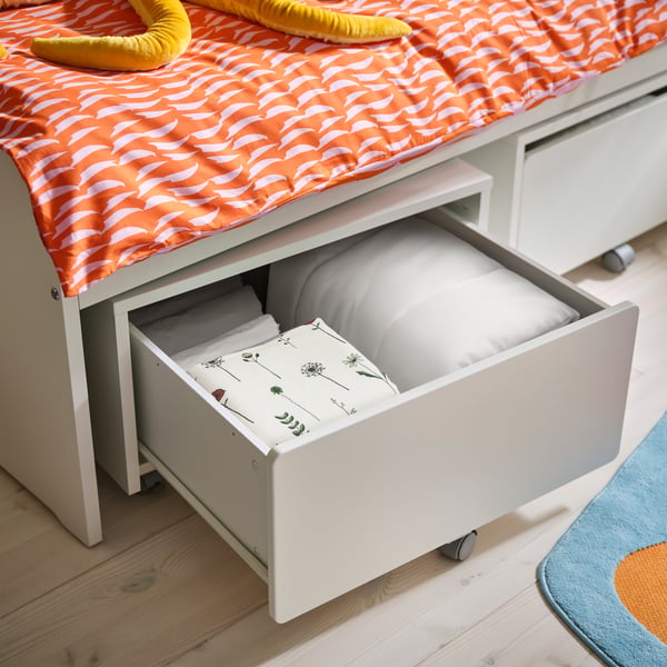 Eine weiße SLÄKT Aufbewahrungsbox mit geöffneter Schublade unter einem Bett.