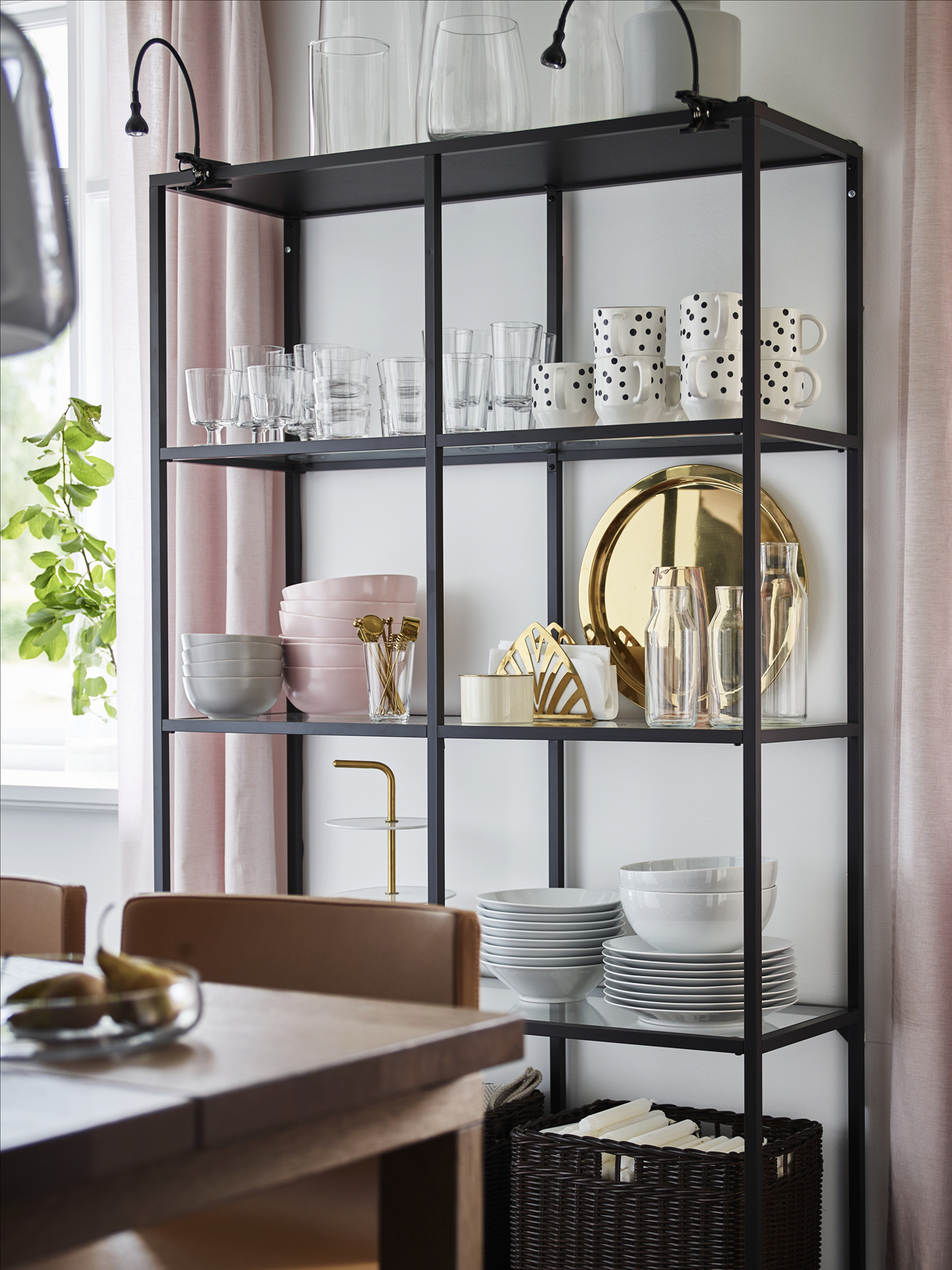 A dining room wall with a black-brown VITTSJÖ shelving unit holding glass and porcelain tableware, and a table with chairs.