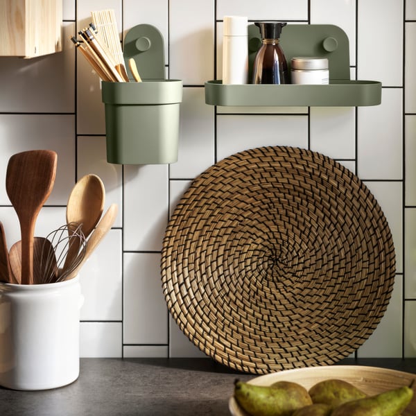 View of a white tiled kitchen wall with an ÖBONÄS wall shelf with suction cup and an ÖBONÄS container with suction cup in gray-green.