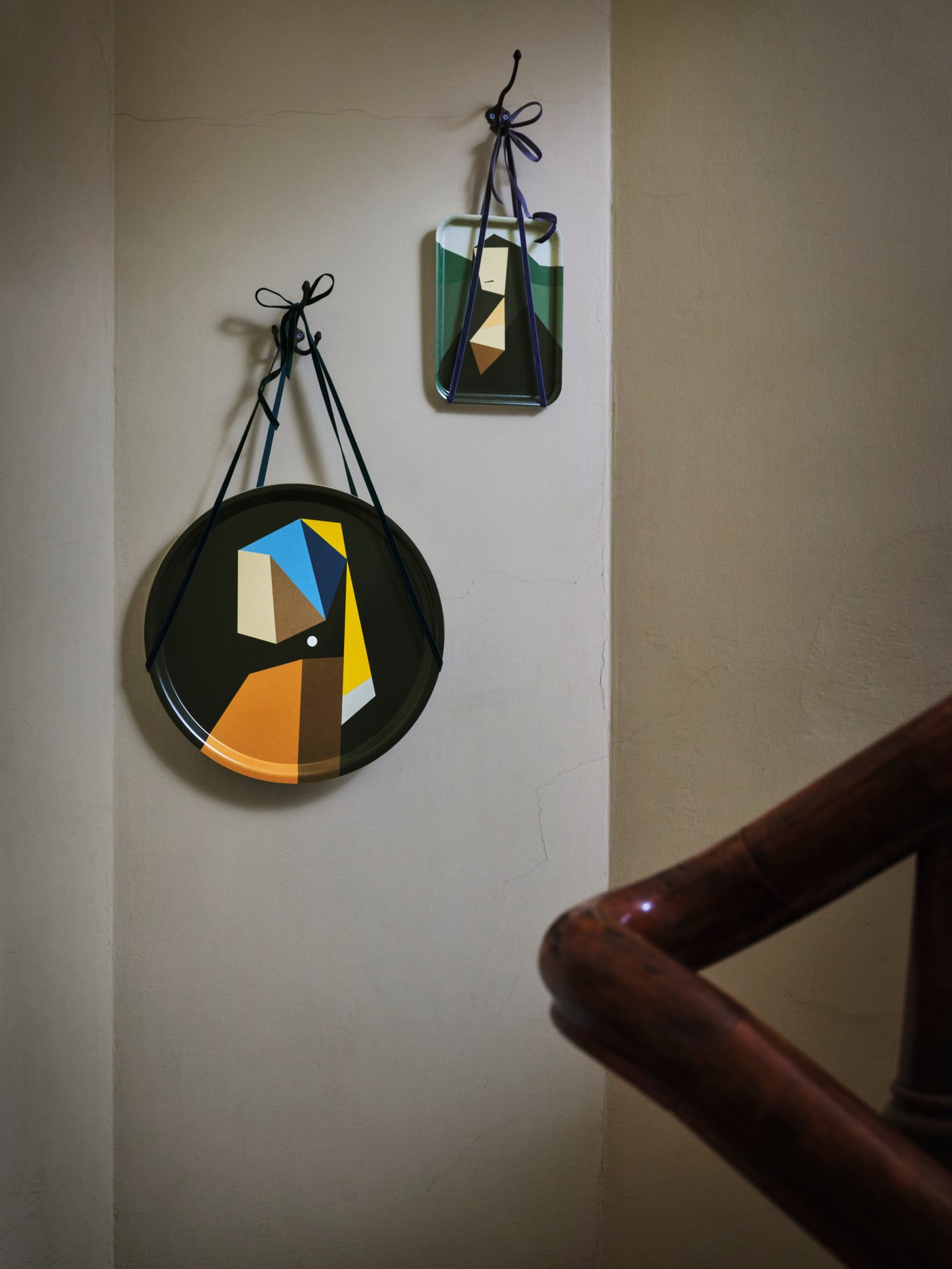 Two DEKORERA trays, with reworked da Vinci and Vermeer motifs, are hung with string side by side on a light brown wall.