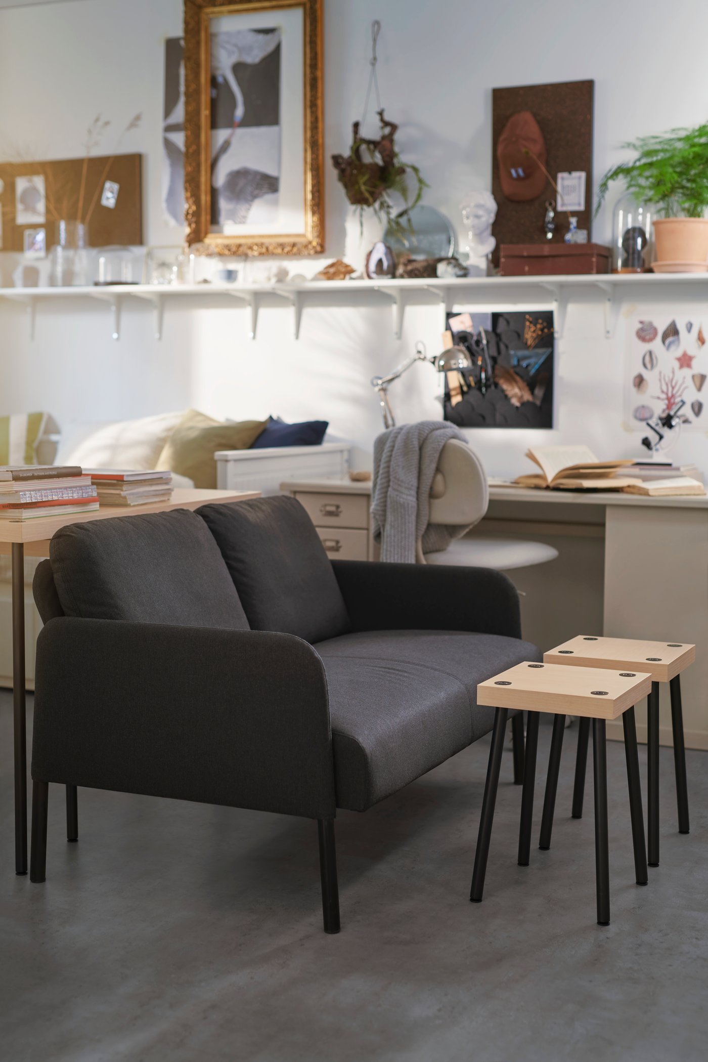 A dark gray GLOSTAD couch sits in a dorm room behind a small wooden coffee table.