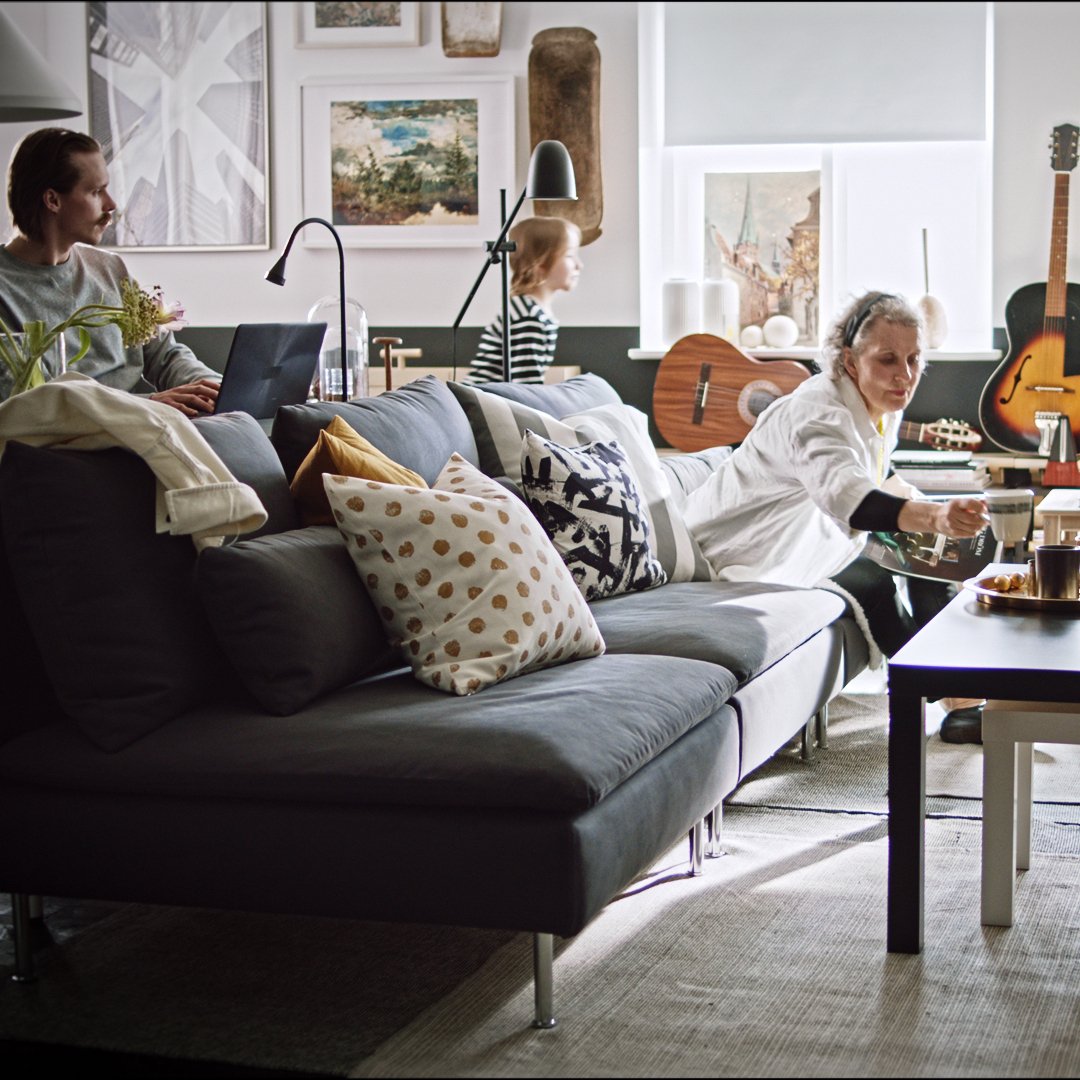 Sillón de la serie SÖDERHAMN con cojines sobre el y una mujer, atras un hombre con su computador y una niña mirando hacia la ventana