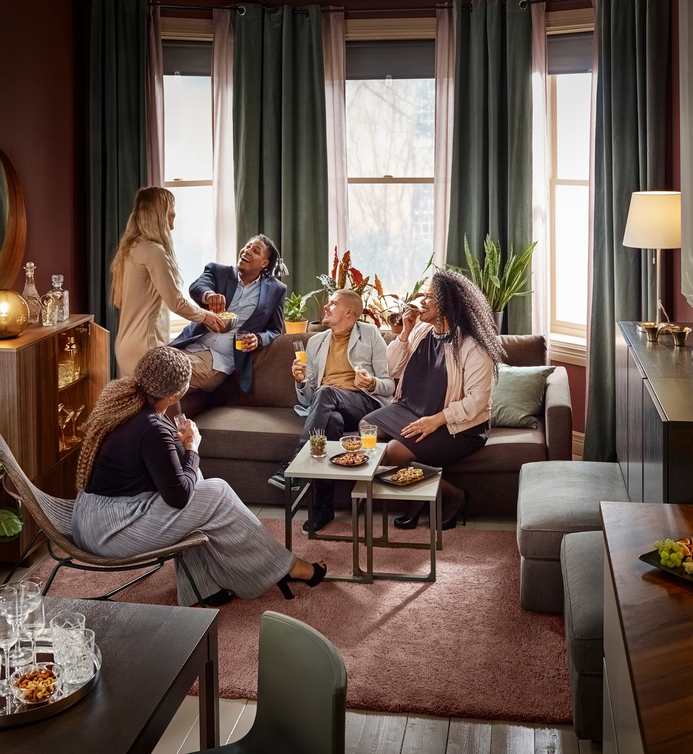 Iluminado living con un sofá junto a la ventana, donde se ven 5 personas compartiendo.