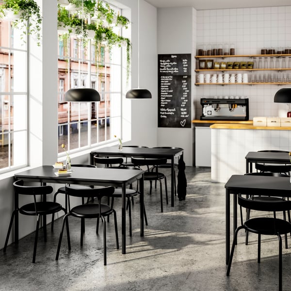 Caféinredning med svarta bord och stolar samt kaffestation.