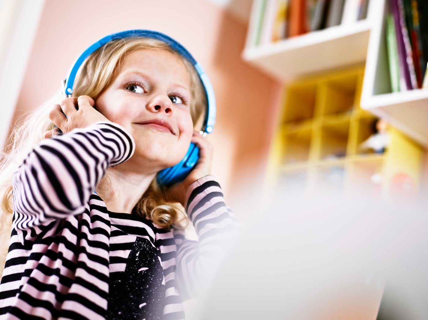 Jeune fille blonde tenant un casque audio bleu au-dessus de sa tête.