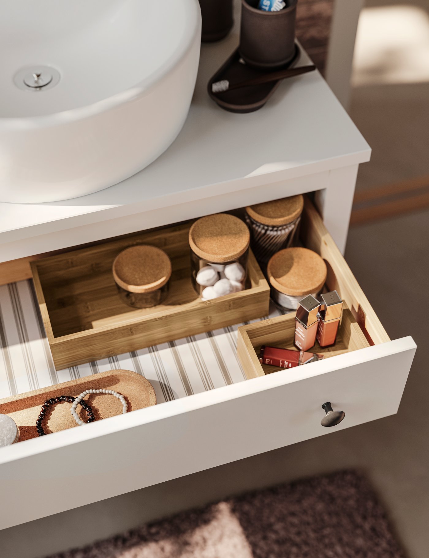 The open drawer of a HEMNES washstand with one drawer in white holding diverse bathroom items and a wash basin in white.