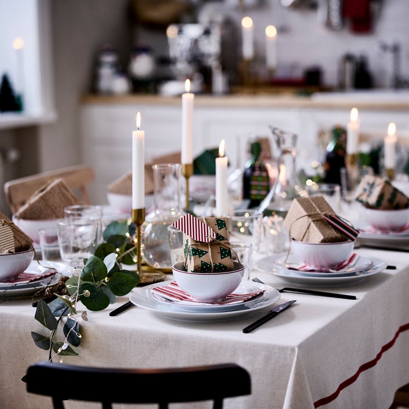 Een gezellige kersttafel is gedekt met VINTERFINT-decoraties, brandende kaarsen en kleine ingepakte cadeautjes in schalen.