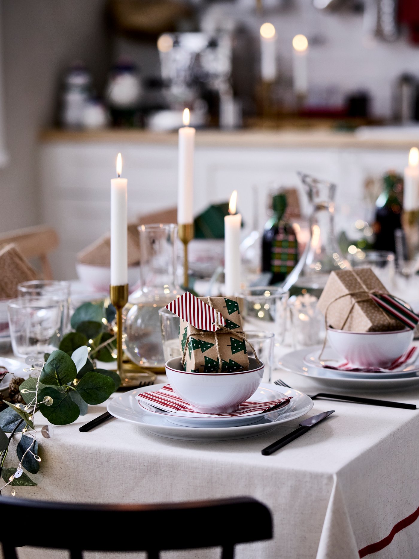 A cosy Christmas table is set with VINTERFINT decorations, lit candles and small wrapped presents in bowls.