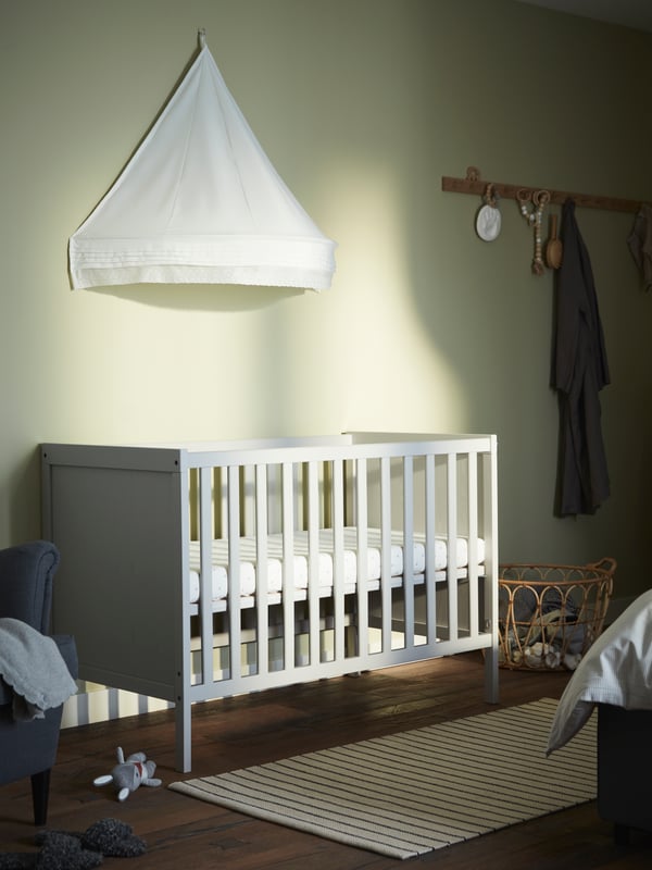 A grey cot, a white bed canopy, a stripe white/black flatwoven rug, oak racks.