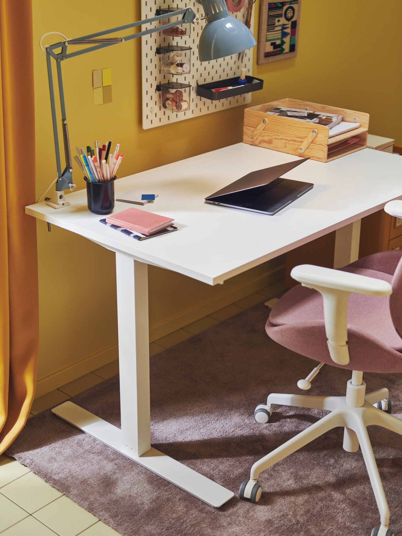 An IKEA TROTTEN white sit/stand desk in a room with yellow walls and purple carpets.