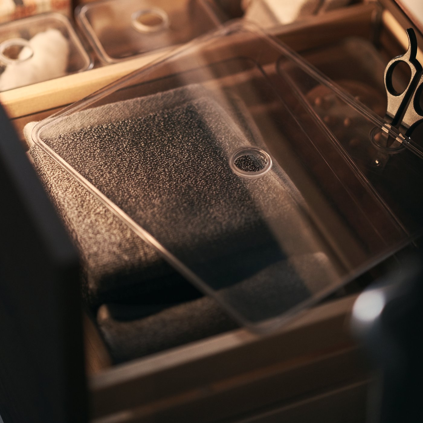 A small GODMORGON box with a clear lid filled with bathroom accessories including scissors.