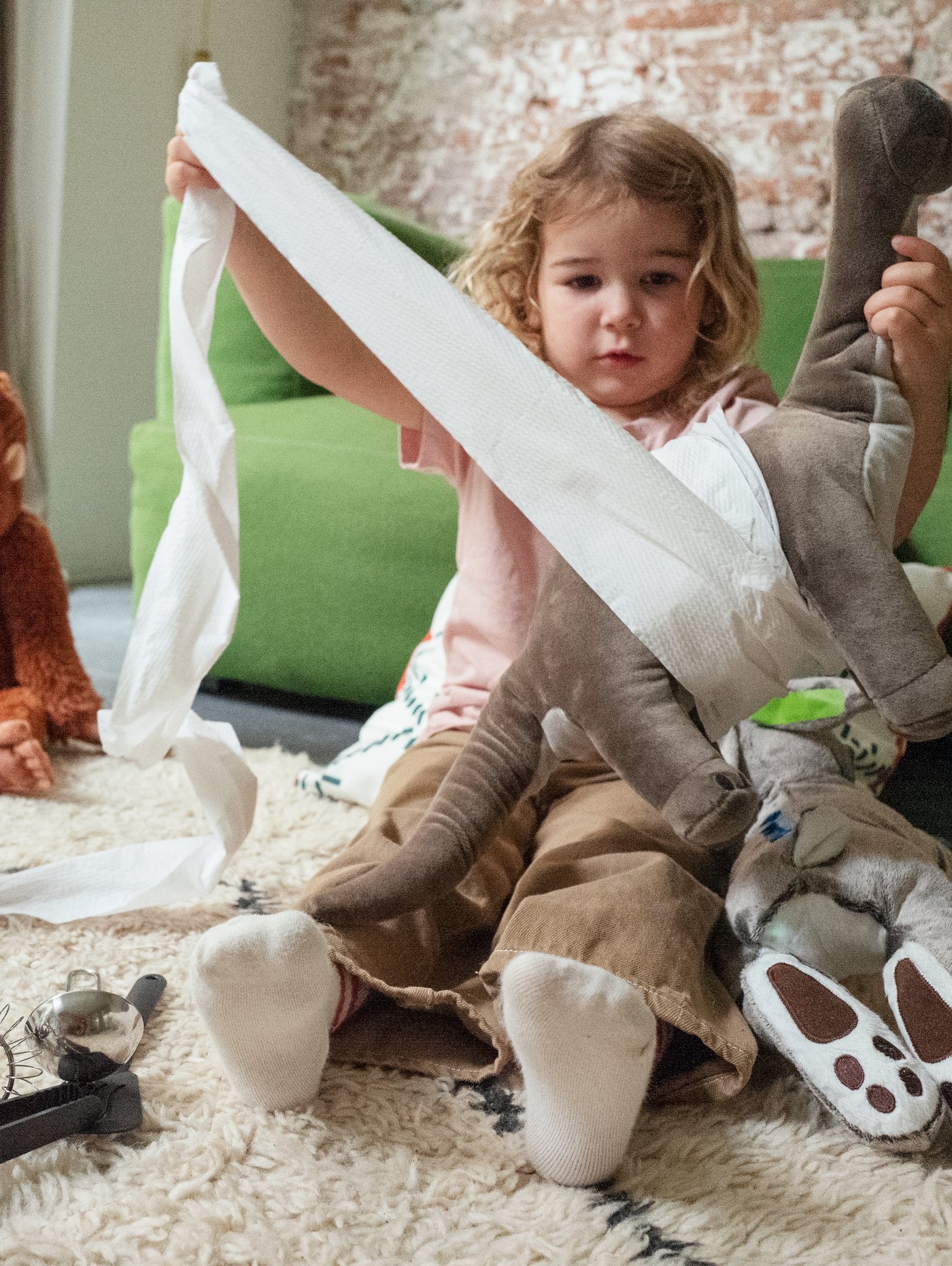 A girl sits in a living room using toilet paper to bandage a JÄTTELIK dinosaur.