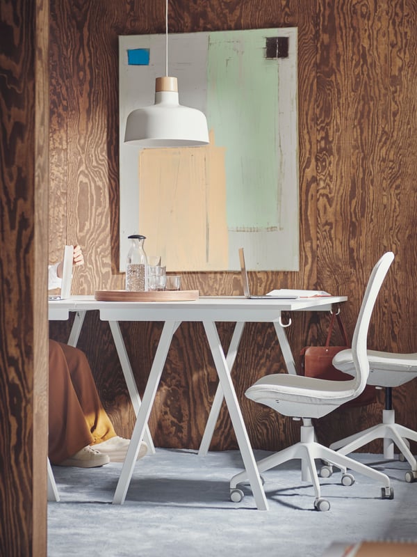 A large BUNKEFLO pendant lamp in white and birch is hanging over a white TROTTEN desk and a couple of white swivel chairs.