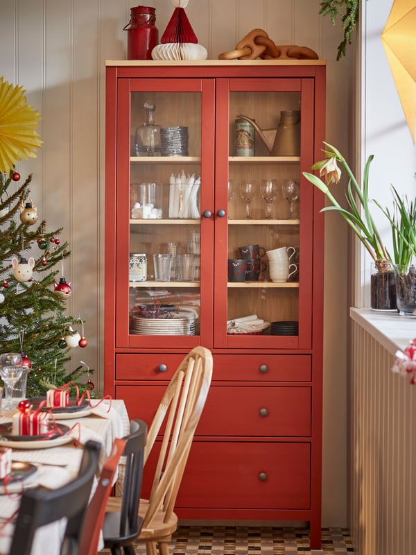 Scandinavian traditional red HEMNES glass cabinet with three drawers in a Swedish dining room decorated for Christmas.