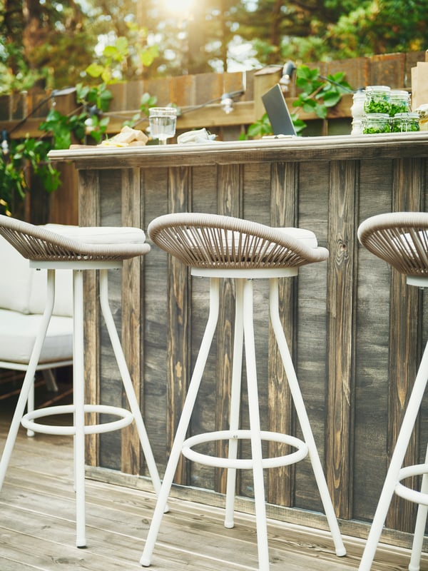 Trois tabourets de bar pivotants SEGERÖN à côté d’un bar en bois où se trouvent un verre, un ordinateur portable et des bocaux avec couvercles contenant des aliments.