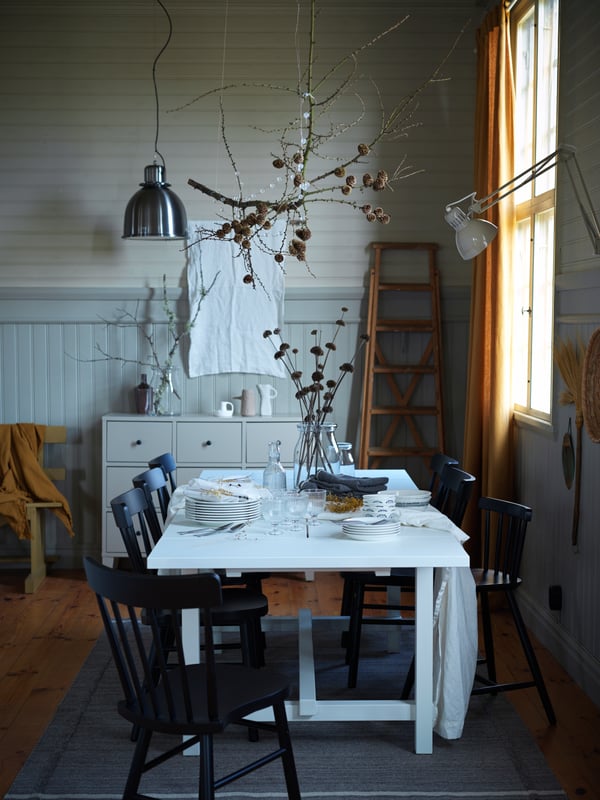 Ein weißer NORDVIKEN Ausziehtisch in einem rustikalen Esszimmer. Der Tisch ist mit einfachem Geschirr und Gläsern eingedeckt.