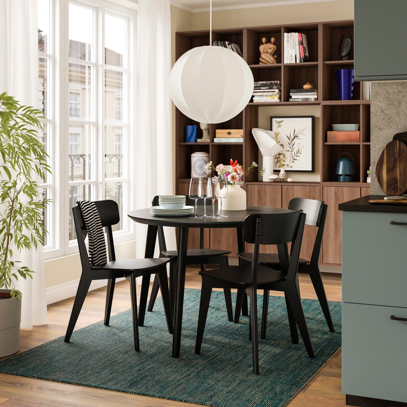 Cozy dining nook with a round black table, four chairs and built‑in shelves by tall windows.