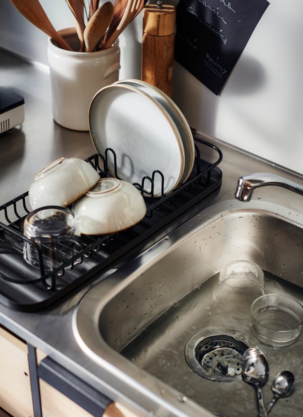 An ÄSPINGE kitchenette with a LILLHAVET multifunctional dish rack in anthracite, with GLADELIG plates and bowls and a glass.