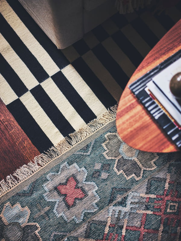 A STOCKHOLM coffee table with walnut veneer placed on a VESTERVIG flatwoven rug and a striped STOCKHOLM flatwoven rug.