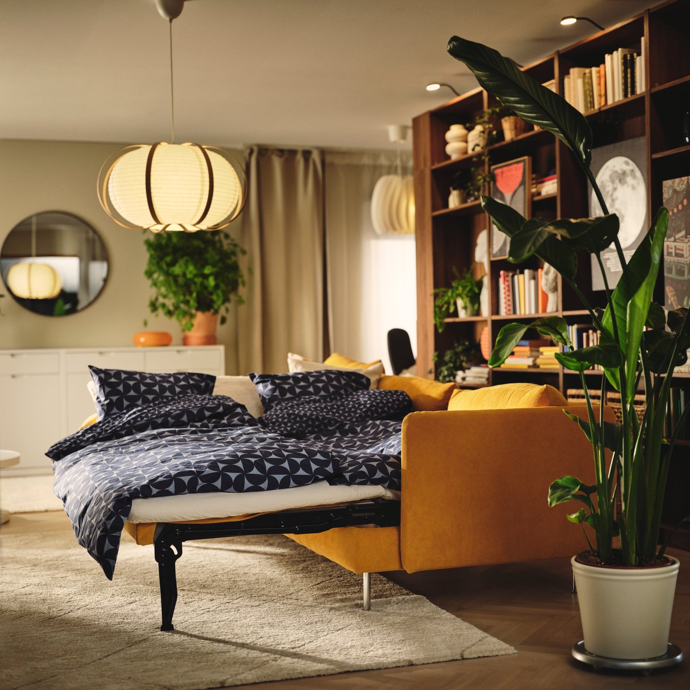 Ein Wohnzimmer mit einem dunkelgelben SÖDERHAMN 3er-Bettsofa, umgeben von Pflanzen und hellen Gardinen.
