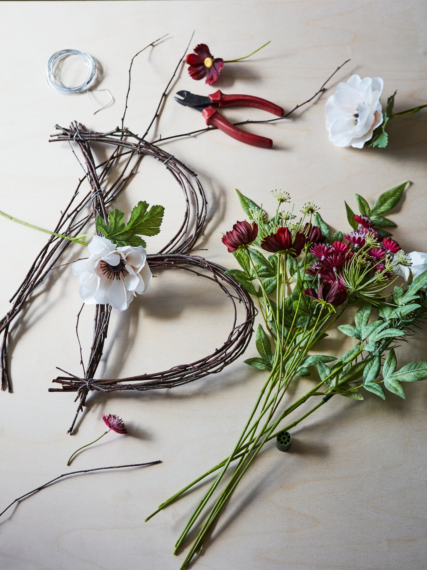 Blomster og grene, der er ved at blive lavet til en blomsterdekoration med bogstavet B på en overflade med en tang.