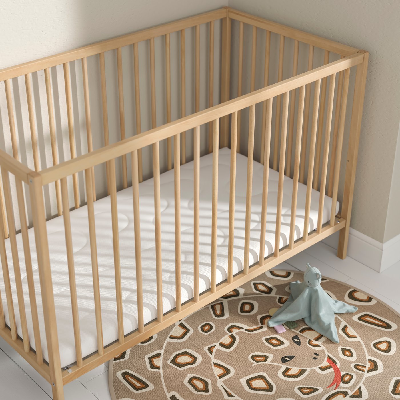 A KRUMMELUR foam cot mattress in a SNIGLAR cot that’s in the corner of a room with a SANDLÖPARE rug on the floor beside it.