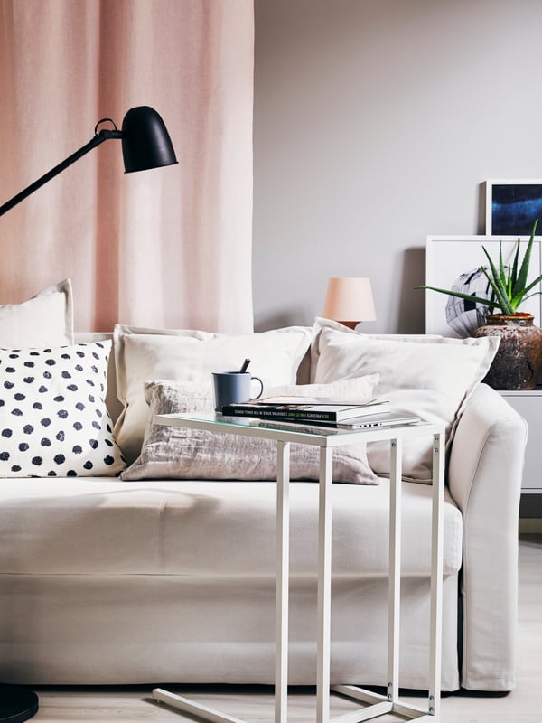 A laptop on a beige BJÖRKÅSEN laptop stand, a jute rug, an armchair with dark grey cushions and a white floor/reading lamp.