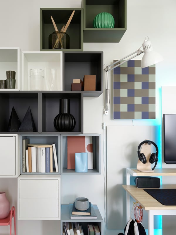 Beside a desk is an asymmetrical grouping of various EKET wall-mounted shelving units that hold modern decor and books.