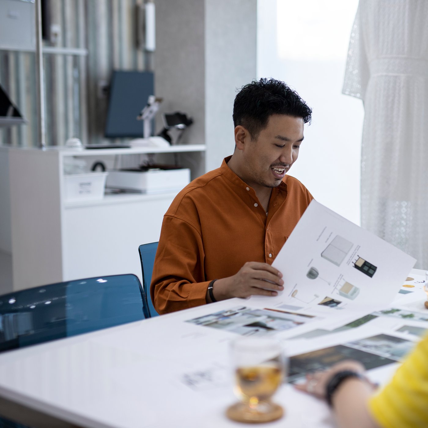 Muškarac koji drži katalog IKEA nameštaja smeši se za stolom s drugima.