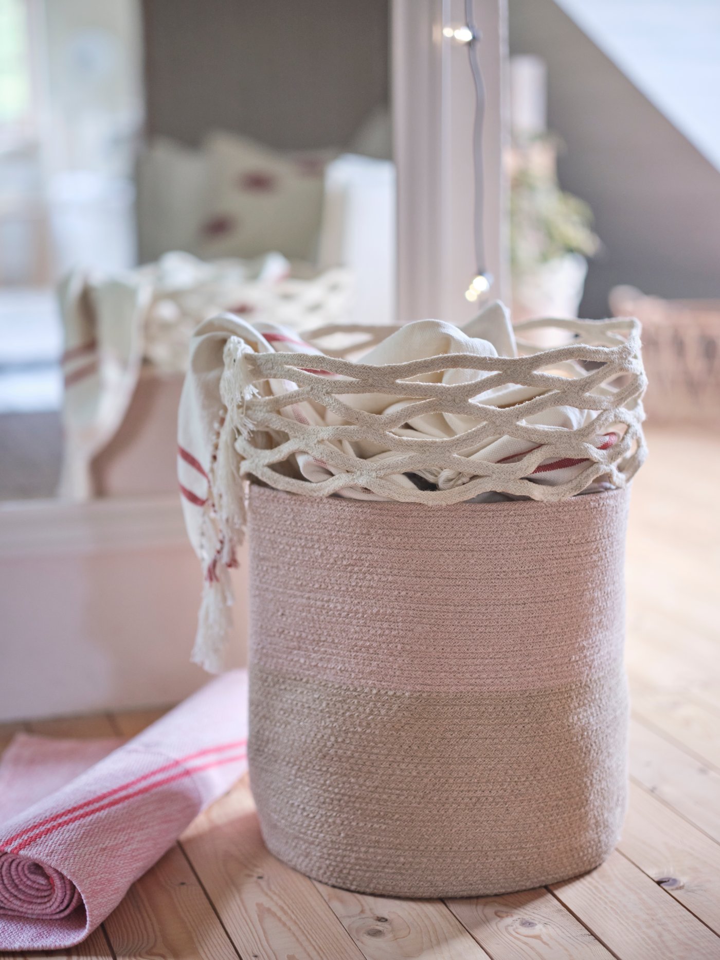 A VÅRDANDE jute storage basket with a woven top and textiles inside and a yoga rug rolled on a wooden floor.