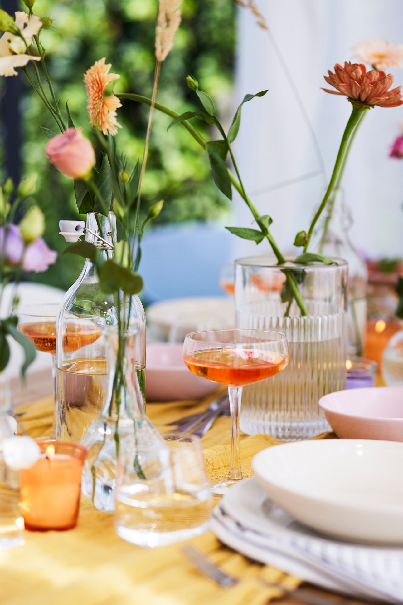 Ein gedeckter Tisch mit Geschirr, verschiedenen Gläsern und mehreren Blumenvasen mit einzelnen Blumen unn Gräsern