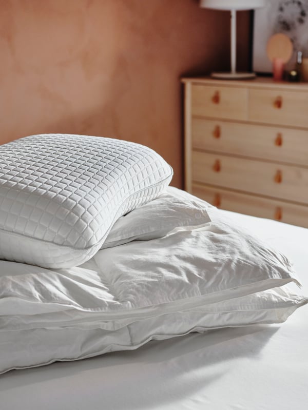Almohada ergonómica KLUBBSPORRE  sobre una cama y un plumón FJÄLLARNIKA.