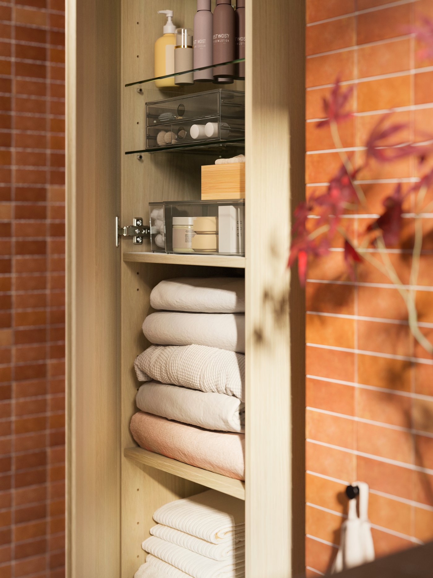 A GODMORGON high cabinet in white oak effect, holding VINARN hand towels and VINARN bath towels in light grey/beige.