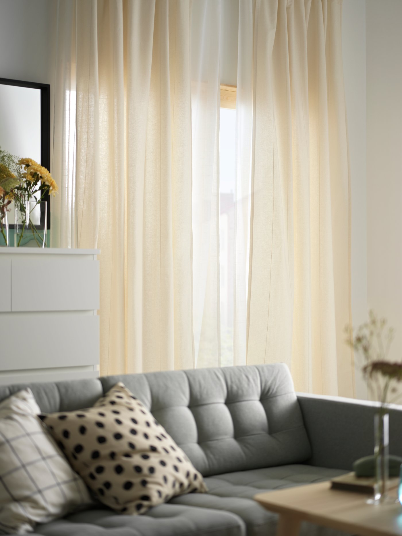 Cortinas LENDA color beige claro colocadas frente a una ventana en una sala, junto a un sofá gris.