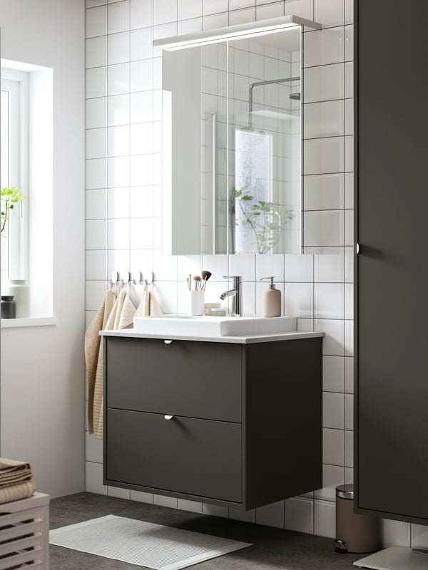 A dark grey HAVBÄCK vanity with two drawers has a tall HAVBÄCK cabinet next to it and a mirror cabinet with above it.