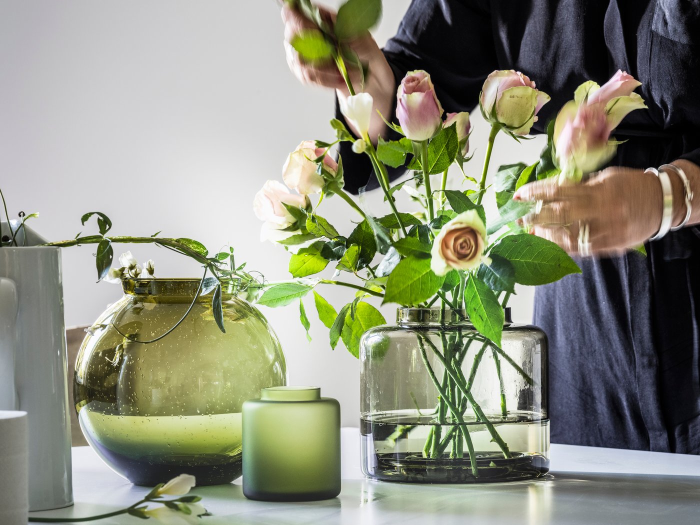 En person arrangerar blommor i en KONSTFULL vas av klarglas som står bredvid ytterligare två KONSTFULL vaser.
