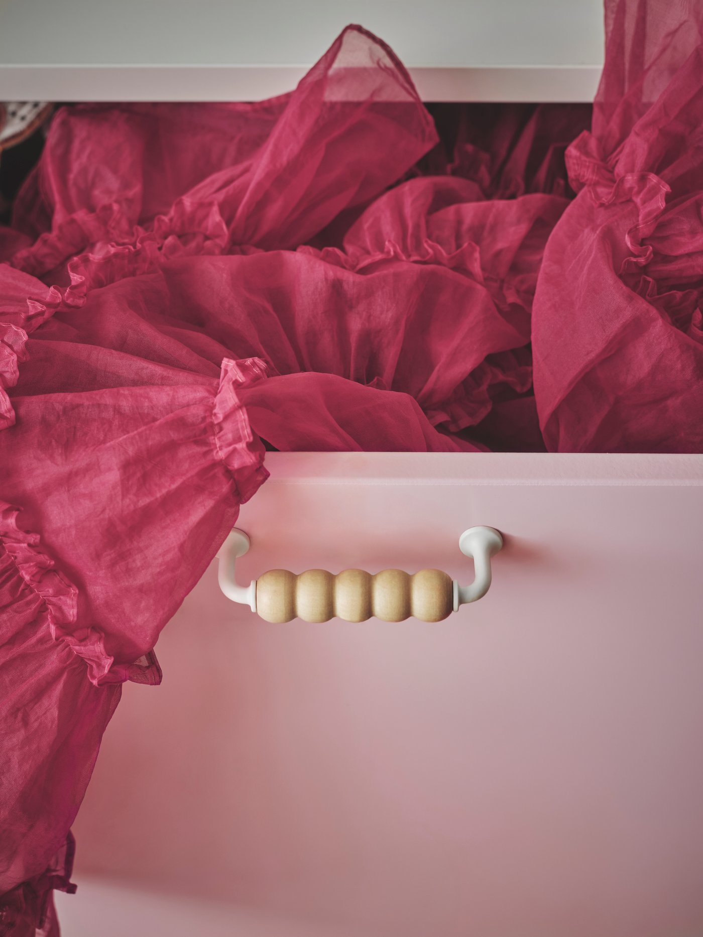 A SMÅSTAD drawer unit with a unique wooden handle placed on a light-pink drawer front with a cerise tulle skirt sticking out.