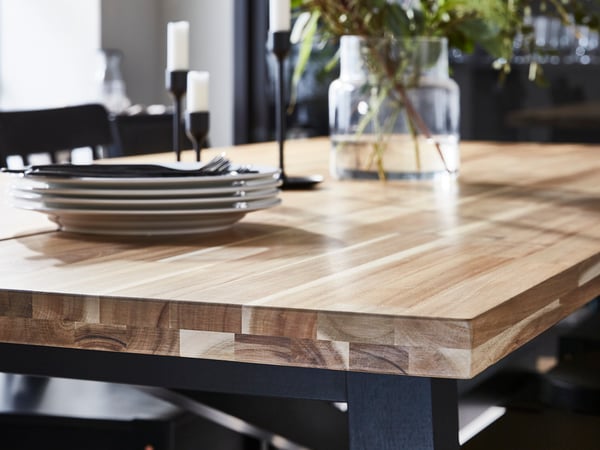 A wood-topped dining table with a striking grain pattern upon which is a pile of dinner plates, some candlesticks and a vase.